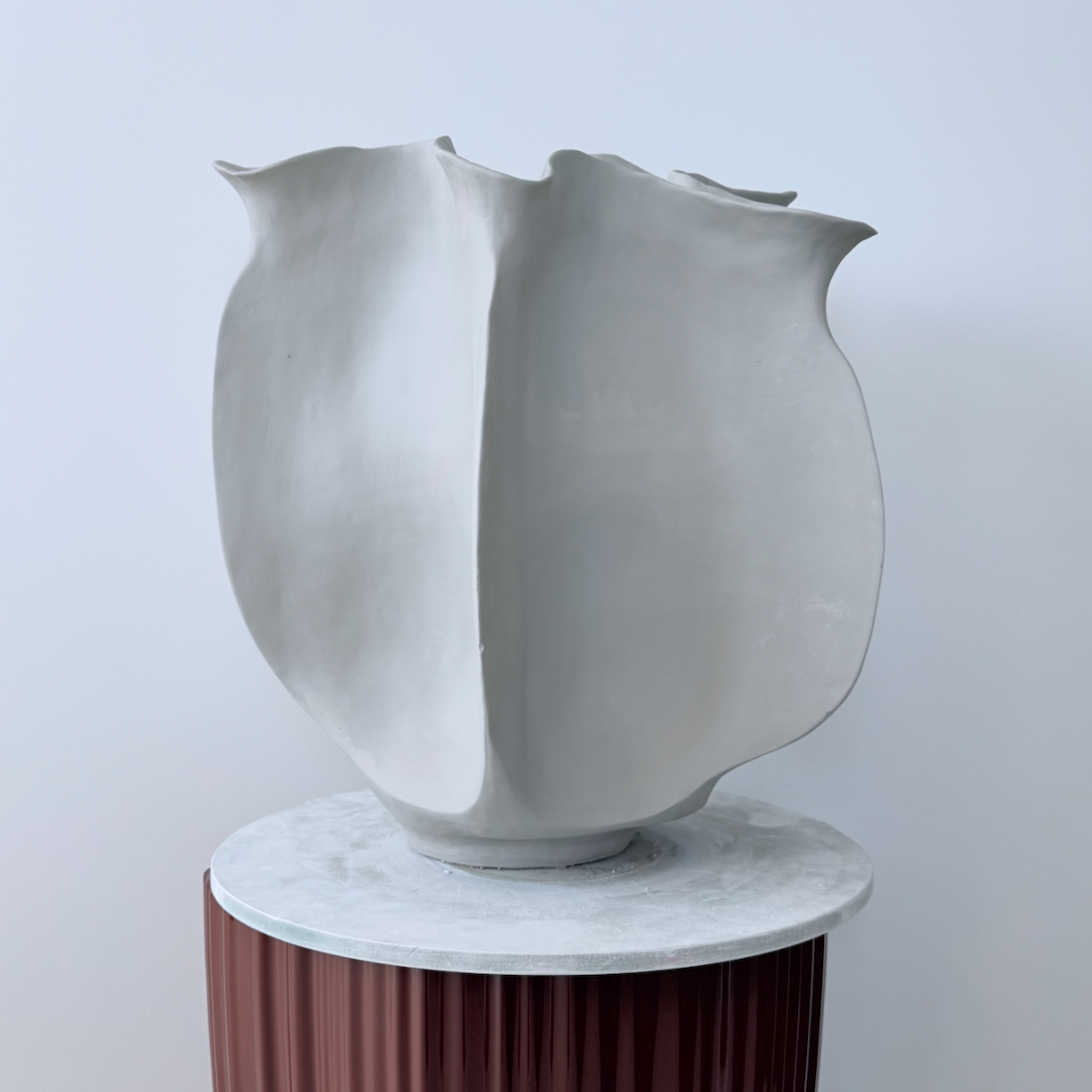 White abstract vase on a cylindrical wooden stand with a white background
